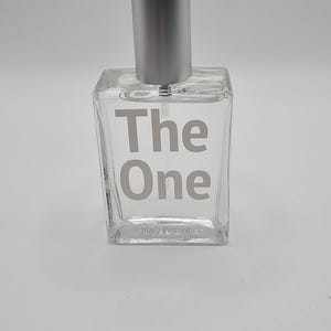 May include: A clear glass perfume bottle with a silver cap. The words "The One" are printed in a light grey colour on the front of the bottle. The brand name "Mary Petford" is printed at the bottom.
