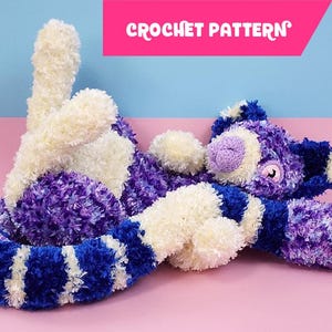 Puede incluir: Un juguete de peluche hecho a mano en tonos morado, blanco y azul, con una textura esponjosa. El juguete tiene apariencia de gato, con cabeza redonda, orejas y cuerpo largo. El texto "CROCHET PATTERN" se muestra en una pancarta rosa.