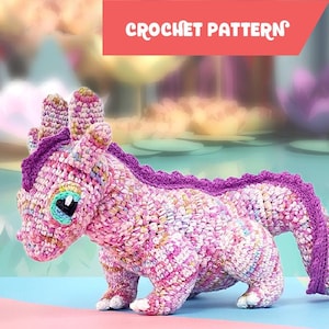 Peut inclure: Un dragon au crochet rose, violet et blanc. Le dragon a un aspect texturé, avec une épine dorsale et une queue violettes. Le texte "CROCHET PATTERN" est affiché dans une bannière rouge au-dessus du dragon.