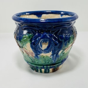 May include: A blue and green ceramic planter with a raised design of a dragon and floral motifs. The planter has a crackled glaze and a slightly distressed look.