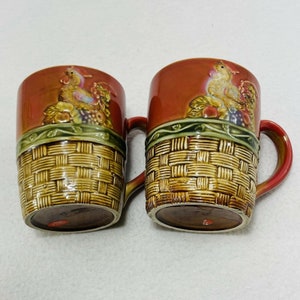 May include: Two ceramic mugs with a brown, green, and yellow woven basket design. The mugs feature a rooster and a hen with fruit and vegetables in the basket.