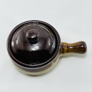 Op de afbeelding: Een bruine en beige keramische ovenschaal met een deksel en een handvat. De schaal heeft een geglazuurde afwerking en is perfect om individuele porties voedsel te serveren.