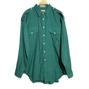 Puede incluir: Una camisa de manga larga a cuadros verdes y blancos con dos bolsillos en el pecho y un puño con un solo botón.