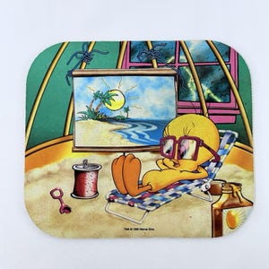 Könnte beinhalten: Ein quadratischer Untersetzer mit Tweety Bird, der sich auf einem Liegestuhl entspannt, eine Sonnenbrille trägt und eine Strandszene betrachtet. Eine Sonnencreme-Flasche und eine Dose sind ebenfalls sichtbar. Der Untersetzer hat einen abgerundeten Rand und einen sandartigen Hintergrund.