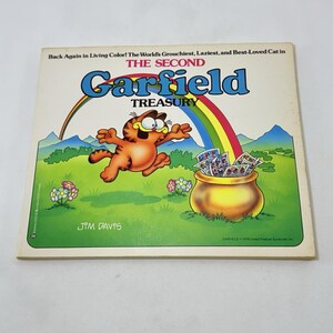 Puede incluir: Portada del libro The Second Garfield Treasury. La portada presenta al personaje de dibujos animados Garfield saltando frente a un arcoíris y una olla de dinero. El texto dice: "Back Again in Living Color! The World's Grouchiest, Laziest, and Best-Loved Cat in The Second Garfield Treasury."