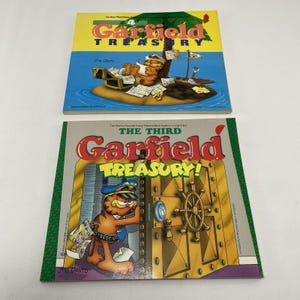 Puede incluir: Dos libros de historietas de Garfield Treasury. El libro de arriba se titula "The 4th Garfield Treasury" y presenta a Garfield sentado en una pequeña isla con un cofre del tesoro. El libro de abajo se titula "The Third Garfield Treasury" y presenta a Garfield con un sombrero de policía y gafas de sol, de pie frente a una gran puerta de la bóveda.
