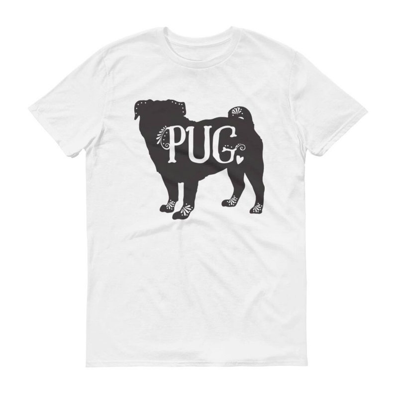 May include: White t-shirt featuring a black silhouette of a pug dog with the word "PUG" in white. The pug design has decorative floral accents. The shirt is made of a soft material.