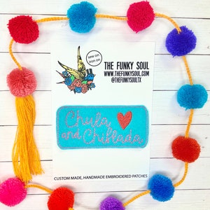 May include: A turquoise blue felt patch with pink stitching, featuring the text "Chula and Chilada" in white cursive font and a red heart. The patch is handmade and embroidered. The text "Sew on iron on" is visible in a circle on a white background.