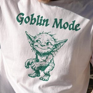 May include: White t-shirt with a green goblin illustration and the words "Goblin Mode". The goblin is smiling. The shirt is size large.