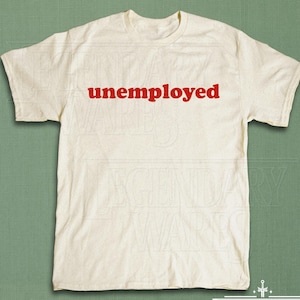 May include: Cream-colored t-shirt with the word "unemployed" printed in red across the chest. The shirt is made of a soft material and has short sleeves and a crew neck. The shirt is a casual wear item.