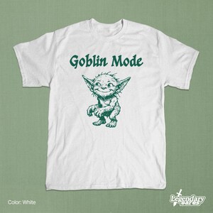 May include: White t-shirt with the text "Goblin Mode" in green above a green cartoon goblin illustration. The goblin has large ears and a mischievous grin. The shirt is a crew neck.