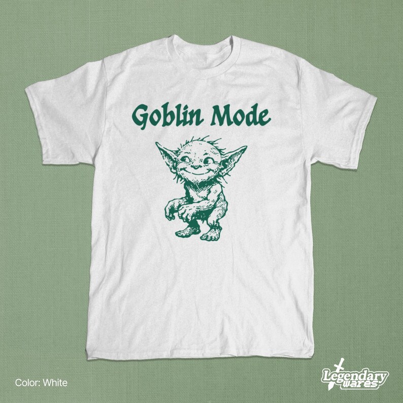 May include: White t-shirt with the text "Goblin Mode" in green above a green cartoon goblin illustration. The goblin has large ears and a mischievous grin. The shirt is a crew neck.