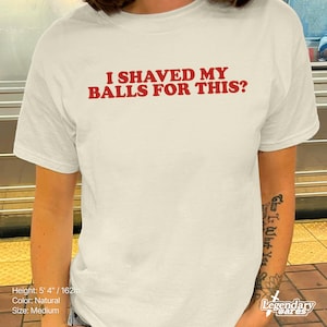 Op de afbeelding: Cr&egrave;mekleurig T-shirt met de rode tekst "I SHAVED MY BALLS FOR THIS?". Het shirt is maat medium en gemaakt van natuurlijk gekleurde stof. De persoon die het shirt draagt, heeft een tatoeage op zijn arm.