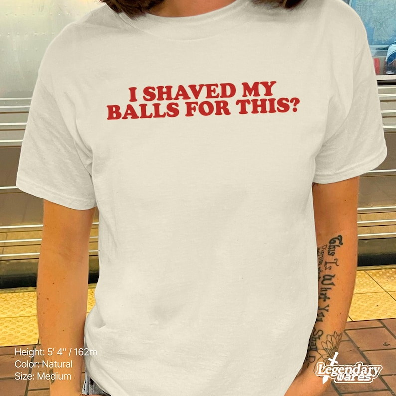 Op de afbeelding: Cr&egrave;mekleurig T-shirt met de rode tekst "I SHAVED MY BALLS FOR THIS?". Het shirt is maat medium en gemaakt van natuurlijk gekleurde stof. De persoon die het shirt draagt, heeft een tatoeage op zijn arm.