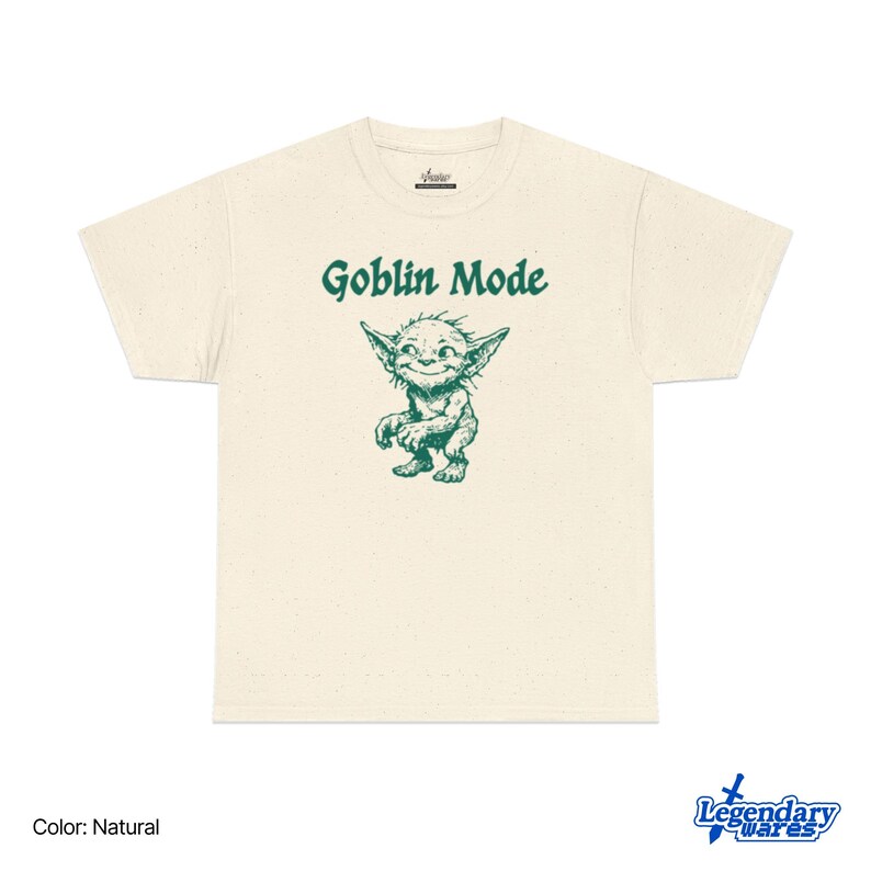 May include: Natural-colored t-shirt with the text "Goblin Mode" above a green cartoon goblin illustration. The goblin has large pointed ears and a mischievous grin. The shirt is made of a soft material.