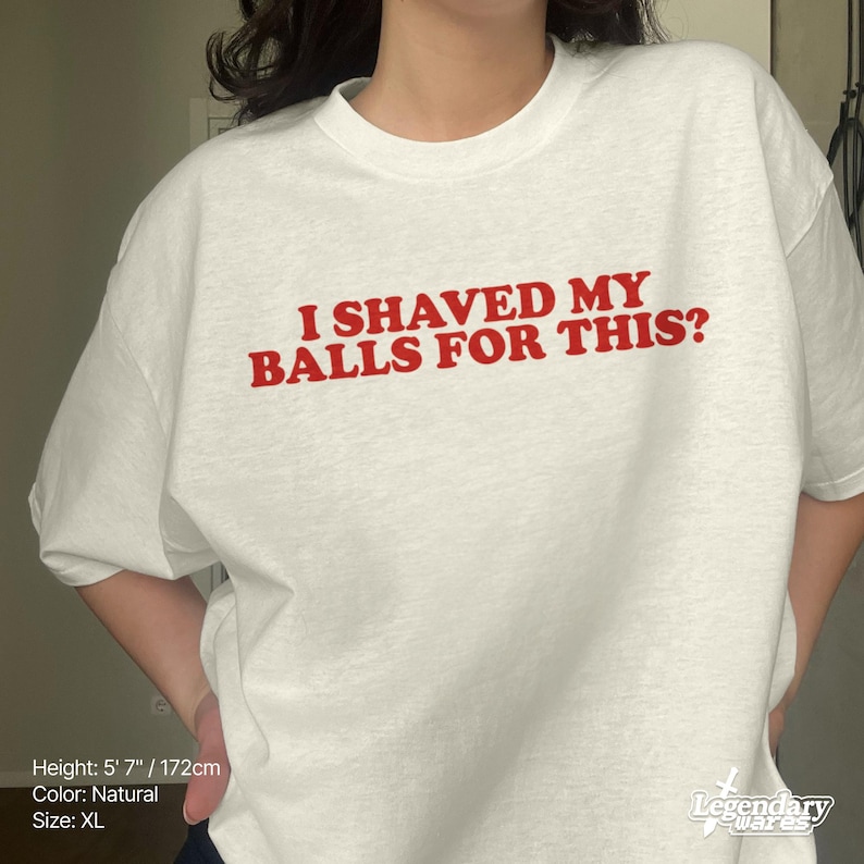 Op de afbeelding: Een natuurlijk gekleurd XL-T-shirt met de tekst "I SHAVED MY BALLS FOR THIS?" in het rood. Het shirt heeft een ronde hals. Het merklogo "Legendary Wares" staat rechtsonder.