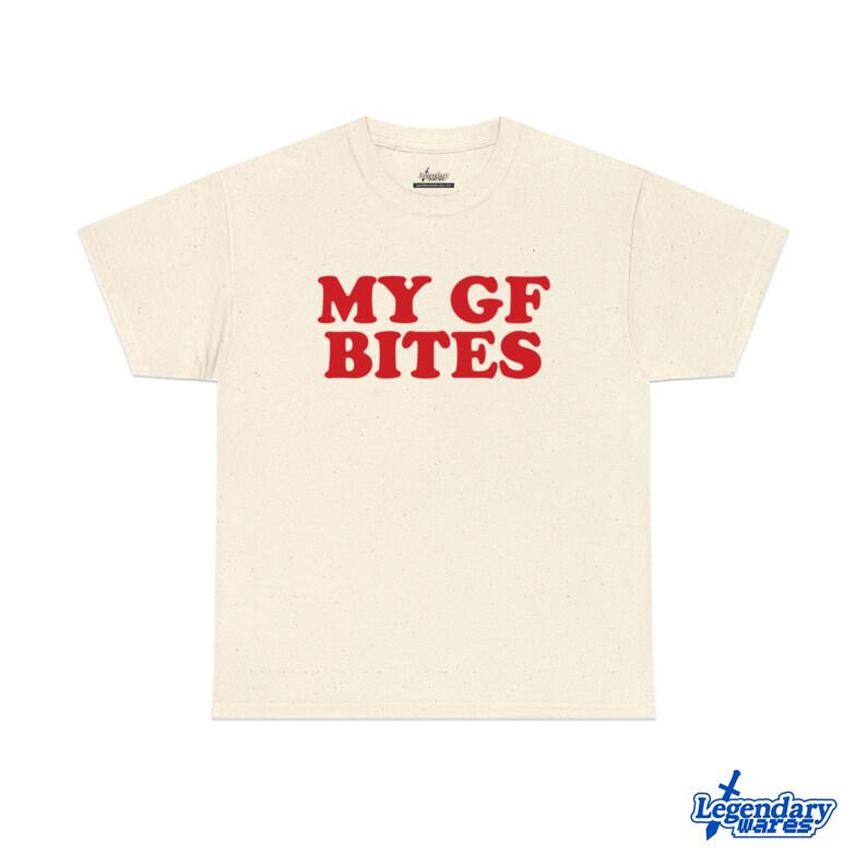 May include: Cream-colored t-shirt with the text "MY GF BITES" in bold red letters. The shirt has a classic crew neck and short sleeves. The shirt is made of a soft, speckled fabric.