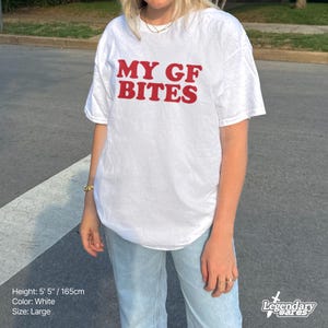 May include: White t-shirt with the red text "MY GF BITES". The shirt is a large size and the model is 5' 5" tall. The shirt is white.