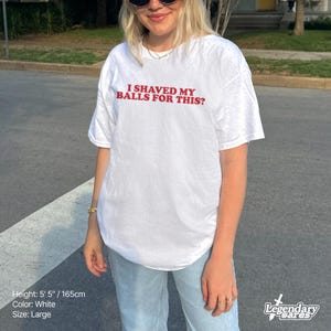 Op de afbeelding: Wit T-shirt met de rode tekst "I SHAVED MY BALLS FOR THIS?". Het shirt is maat large en de persoon op de foto is 165 cm lang. Het shirt is wit.