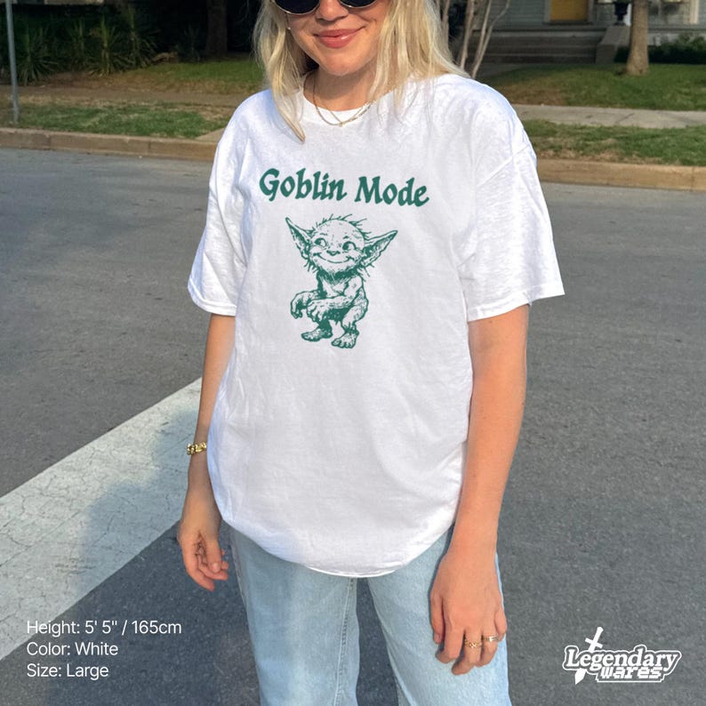 May include: White t-shirt with the text "Goblin Mode" above a green cartoon goblin illustration. The shirt is a large size and the model is 5' 5" tall. The shirt is from Legendary Wares.