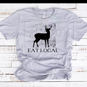 Puede incluir: Una camiseta gris con una silueta negra de un ciervo en un rectángulo desgastado con el texto "EAT LOCAL" debajo.