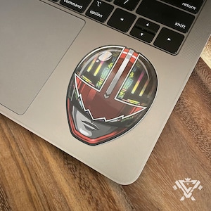 May include: A red and black helmet with a red visor and a silver stripe down the middle. The helmet has a detailed design with a holographic effect.