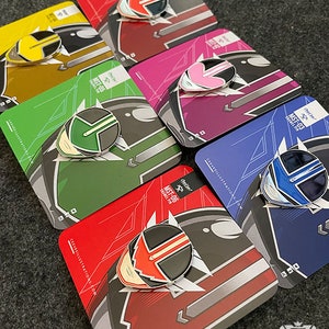 Könnte beinhalten: Sechs Emaille-Pins mit verschiedenen farbigen Ranger-Helmen aus dem Power Rangers-Franchise. Die Pins werden auf ihren individuellen Rückseitenkarten angezeigt, jede mit dem Text "Crete! MST-06 GRAMEL PIN" und "CEEVEEILLUSTRATIONs.com".