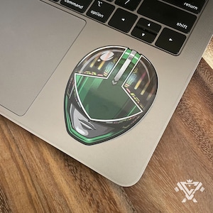 May include: Green Power Ranger helmet sticker with a detailed design and a black background.