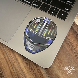 May include: A blue and silver Power Ranger helmet sticker with a detailed design. The helmet has a visor and a face with a serious expression.