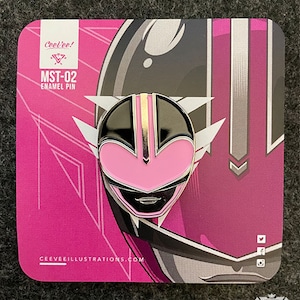 May include: Pink, black, and gold enamel pin of a helmet design, labeled "MST-02". The pin is on a pink card with the text "CeeVee!" and "CEEVEEILLUSTRATIONS.COM". The design features a stylized helmet with white accents.