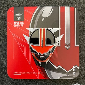Könnte beinhalten: Ein rot-schwarz-weißer Emaille-Pin mit Helmdesign, bezeichnet als MST-06. Der Pin befindet sich auf einer rot-schwarzen Rückkarte mit dem Text "CeeVee!" und "CEEVEEILLUSTRATIONS.COM". Der Pin hat einen roten Mittelstreifen und weiße Akzente.