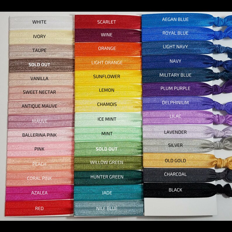 May include: A set of 24 colorful hair ties with glitter, arranged in two columns. The hair ties are labeled with names like "White", "Scarlet", "Aegian Blue", "Ivory", "Wine", "Royal Blue", "Taupe", "Orange", "Light Navy", "Sold Out", "Light Orange", "Navy", "Vanilla", "Sunflower", "Military Blue", "Sweet Nectar", "Lemon", "Plum Purple", "Antique Mauve", "Chamois", "Delphinium", "Mauve", "Ice Mint", "Lilac", "Ballerina Pink", "Mint", "Lavender", "Pink", "Sold Out", "Silver", "Peach", "Willow Green", "Old Gold", "Coral Pink", "Hunter Green", "Charcoal", "Azalea", "Jade", "Black", "Red", "Nile Blue".