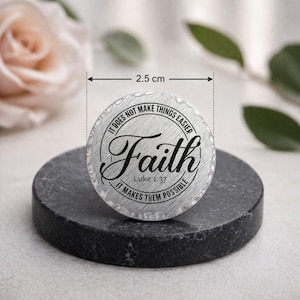 May include: A circular, silver-toned metal item, 2.5 cm across, featuring the word "Faith" in cursive. The text "IT DOES NOT MAKE THINGS EASIER" and "IT MAKES THEM POSSIBLE" are around the edge, with "Luke 1:37" beneath "Faith".