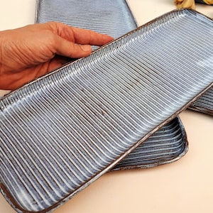 May include: Rectangular ceramic serving platters with a textured, ribbed surface. The platters are a muted blue-gray color with white accents and dark brown edges. The handmade dishes are ideal for serving appetizers or small dishes.