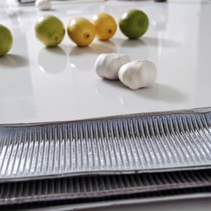 May include: Two rectangular, blue and gray ceramic serving platters with a ribbed texture. The platters are stacked on top of each other. There are limes and lemons on a white surface in the background.