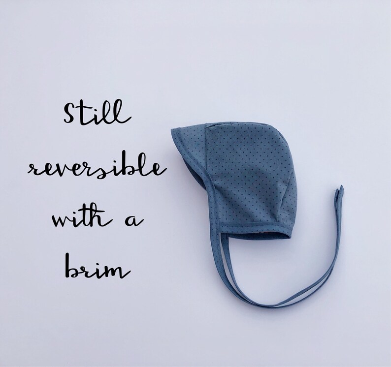 May include: A blue baby bonnet with white polka dots and ties. The bonnet is reversible and has a brim. The text "still reversible with a brim" is written on a white background.
