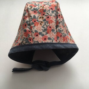 May include: A floral print surgical cap with a navy blue trim and tie. The cap features a pink and white floral pattern.