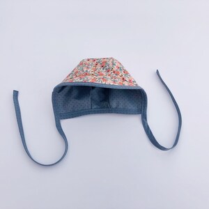 May include: A blue baby bonnet with a floral print and tie strings.