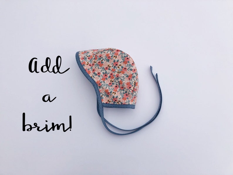 May include: A baby bonnet with a floral print and blue ties. The text "Add a brim!" is written in black on a white background.
