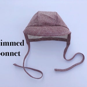 May include: A brown, brimmed bonnet with a tie. The bonnet is made of a soft, textured fabric.