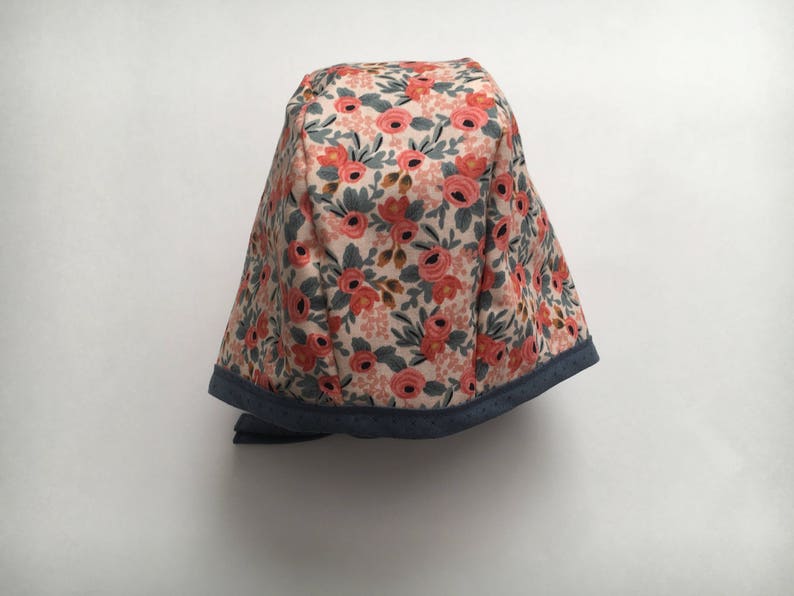 May include: A floral print fabric hat with a blue trim. The hat has a rounded shape and a tie.