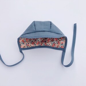 May include: A blue baby bonnet with a floral print lining. The bonnet has two ties that can be tied under the chin.