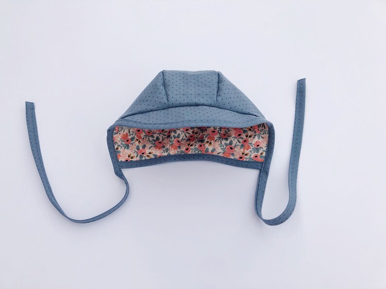 May include: A blue baby bonnet with a floral print lining. The bonnet has two ties that can be tied under the chin.