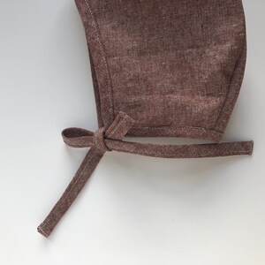 May include: A brown linen baby bonnet with a tied bow at the back.