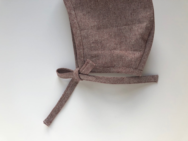 May include: A brown linen baby bonnet with a tied bow at the back.