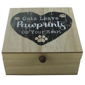 Peut inclure: Une boîte en bois avec un motif en forme de cœur sur le couvercle. Le cœur est noir avec des empreintes de pattes blanches et le texte "Cats Leave Pawprints On Your Heart".