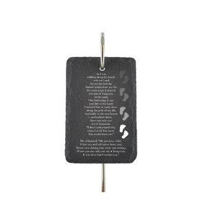 May include: A rectangular, dark gray slate plaque with a poem and footprints etched into the surface. The plaque is suspended by a silver-colored metal ring and rod. The text is in a vertical format.