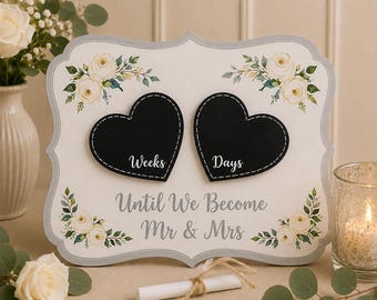 May include: A decorative white wooden sign with a scalloped edge, featuring two black heart-shaped chalkboards labelled Weeks and Days. The text Until We Become Mr & Mrs is printed in grey, accented by illustrations of white roses and green leaves.