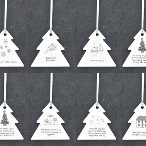 May include: Set of ten white ceramic Christmas tree ornaments with various holiday-themed illustrations and text. The ornaments feature sayings like "Baby's First Christmas", "Deck the Halls", and "Family is everything at Christmas and always".
