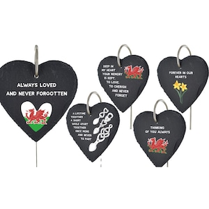 May include: Five black heart-shaped slate garden markers with metal rings and stakes. Each marker features a different Welsh dragon design and a sentimental message. The messages include "Always Loved and Never Forgotten", "Deep in my heart your memory is kept. To love, to cherish and never forget", "A lifetime together a short while apart together once more and never to part", "Forever in our hearts", and "Thinking of you always".